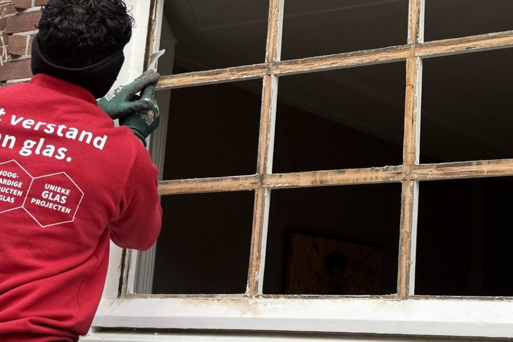 Glaszetter vervangt glas in een oud houten roedenraam met behoud van karakter